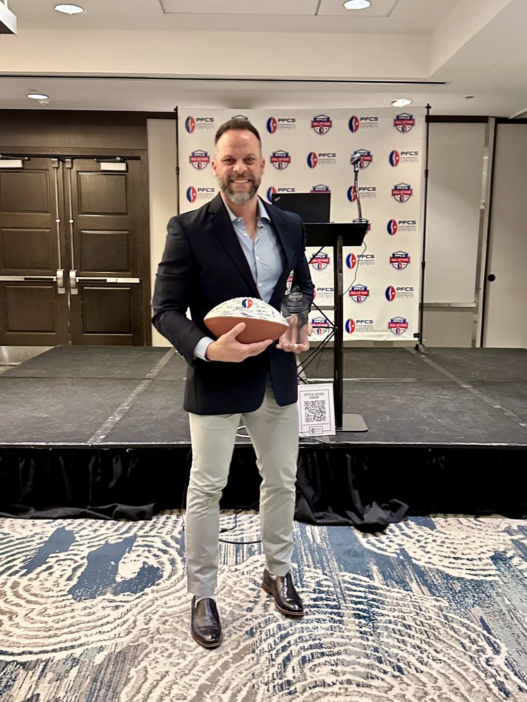 Dr. Joseph Krzemien holding the PFCS Hall of Fame crystal trophy and signed Class of 2025 induction football
